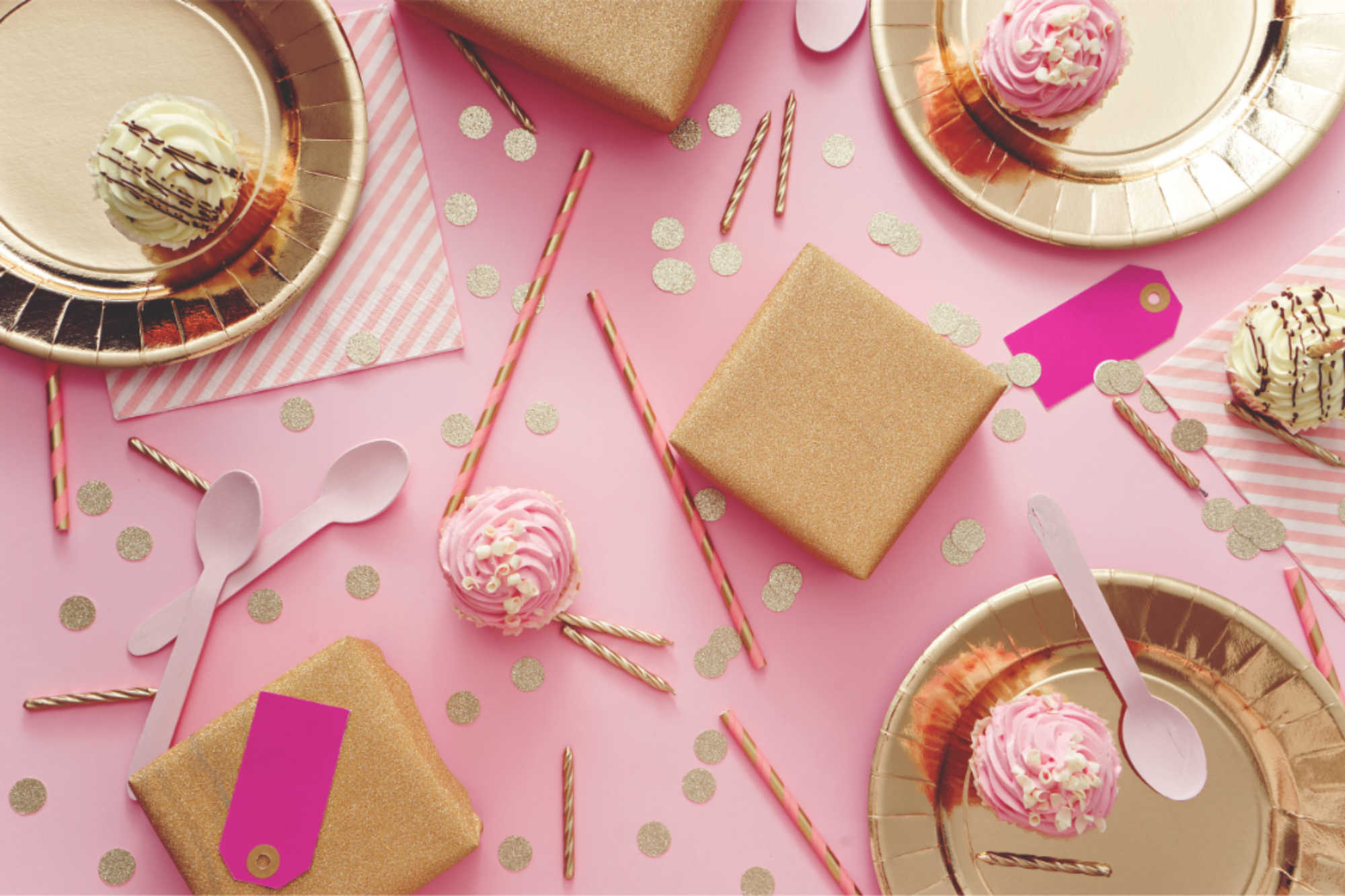 A pink table covered with gold plates, gold napkins, and confetti in various shades of gold and pink.