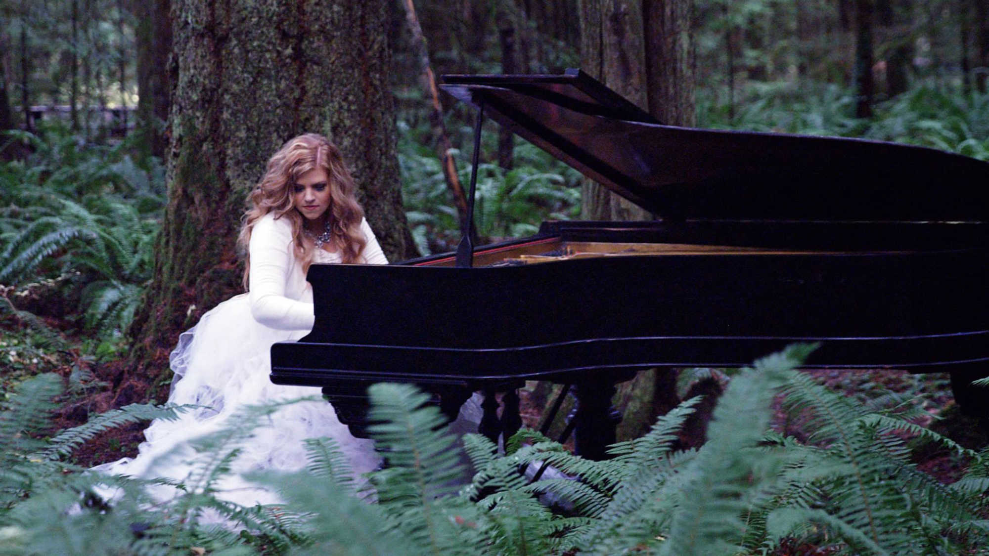 Jennifer Thomas, pianist, films a music video playing a piano in the forest.